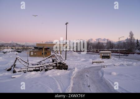 Paysage enneigé près de l'aéroport de Merrill Field à Anchorage, Alaska, présentant un champ enneigé avec un avion lointain et une montagne majestueuse en toile de fond. Une scène hivernale sereine symbolisant la tranquillité et l'isolement pendant les mois froids. Banque D'Images