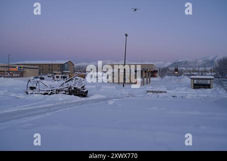 Paysage enneigé serein près de l'aéroport de Merrill Field à Anchorage, Alaska. Un avion vole au-dessus de vous, symbolisant voyage et aventure au milieu d'une scène hivernale tranquille. La neige couvre les bâtiments et les environs, créant une atmosphère paisible et glacée. Banque D'Images