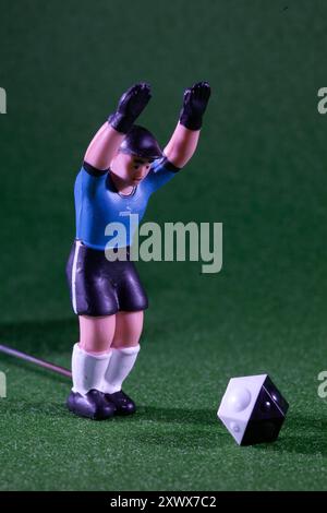 Gros plan d'une figure de joueur de football jouet levant ses bras en célébration sur un terrain vert. La figurine se tient à côté d'un dé au design unique, capturant l'excitation et le plaisir des jeux de table. Banque D'Images