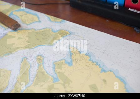 Vue rapprochée d'une carte nautique détaillée placée sur un bureau en bois, représentant les zones côtières et les voies navigables. Idéale pour ceux qui s’intéressent à la navigation, à l’exploration ou aux études maritimes, cette image transmet un sentiment d’aventure et de découverte. Banque D'Images