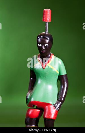 Gros plan d'une figurine de footballeur Tipp-Kick vêtue des couleurs du maillot de l'équipe nationale du Cameroun. La figure présente une tenue verte et rouge sur fond vert. Adapté aux concepts sportifs. Banque D'Images