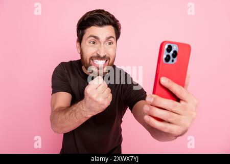 Photo d'un gars agressif dangereux avec un t-shirt brun habillé de trois jours look au smartphone jetant poing isolé sur fond de couleur rose Banque D'Images