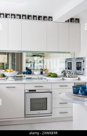 Cuisine blanche moderne avec splashback miroir dans une maison élégante à Londres, Royaume-Uni Banque D'Images