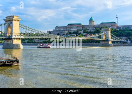 Budapest, Hongrie - 7 juillet 2024 : Pont des chaînes avec un bateau passant sur le Danube, mettant en valeur l'architecture emblématique de Budapest. Banque D'Images