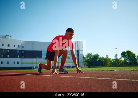 Photo à angle bas du jeune homme, prêt à courir debout sur la ligne de départ en position de départ basse. Réalisations et motivation. Banque D'Images