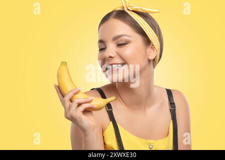 Portrait d'une belle fille brune avec une peau saine et propre et maquillage frais sur un fond jaune. Elle tient une banane. Concept de nutrition saine. Banque D'Images