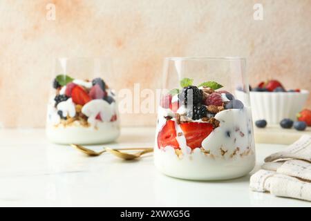 Yaourt savoureux avec baies fraîches, granola et menthe dans des verres servis sur une table blanche Banque D'Images