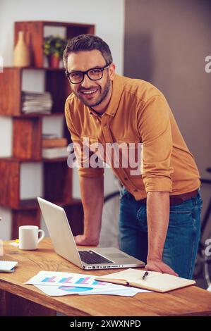 Rester positif dans n'importe quelle situation. Beau jeune homme regardant la caméra et souriant tout en se tenant près de son lieu de travail au bureau Banque D'Images