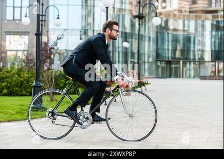 Passe partout par son vélo. Vue latérale du jeune homme d'affaires à l'avant en roulant sur son vélo Banque D'Images