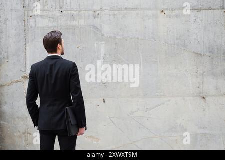 Face à un mur. Vue arrière d'un jeune homme tenant une mallette tout en se tenant debout à l'extérieur et contre le mur de béton Banque D'Images