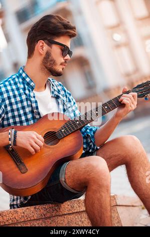 Il adore ce son. Vue à angle bas de beau jeune homme jouant de la guitare tout en dehors Banque D'Images