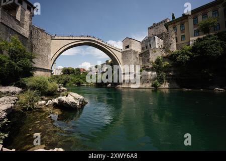 L'emblématique pont Stari Most à Mostar, en Bosnie, s'étend sur la rivière Neretva au milieu d'une architecture historique et d'une verdure vibrante par une journée ensoleillée. Banque D'Images