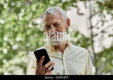 Un homme d'âge mûr avec une barbe vérifie son téléphone tout en se tenant dehors. Banque D'Images