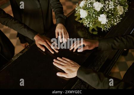 Plan à angle élevé de mains biraciales méconnaissables sur cercueil à côté d'un bouquet de roses blanches Banque D'Images