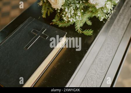 Bible avec croix sur couverture en cuir noir et bouquet de roses sur cercueil en bois noir Banque D'Images