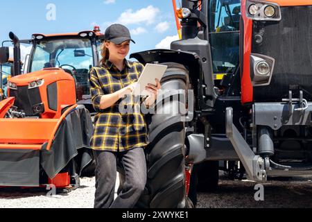 Représentant des ventes d'une concession de machines agricoles et de construction se tient à côté d'un tracteur et utilisant une tablette numérique. Banque D'Images