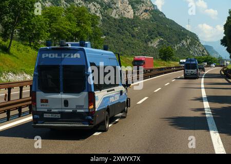 Ossenigo, Italie - 8 juin 2023 : les forces de l'ordre se déplacent sur une autoroute très fréquentée, flanquée de verdure luxuriante et de montagnes imposantes sous un bleu clair Banque D'Images