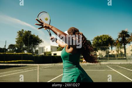 Joueuse de tennis vue de derrière, frappant une volée sur un terrain dur pendant une journée ensoleillée. Femme sportive jouant au tennis en plein air. Banque D'Images