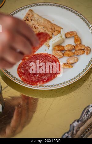 ramasser à la main salami, fromage, craquelins, amandes sur une assiette fantaisie Banque D'Images