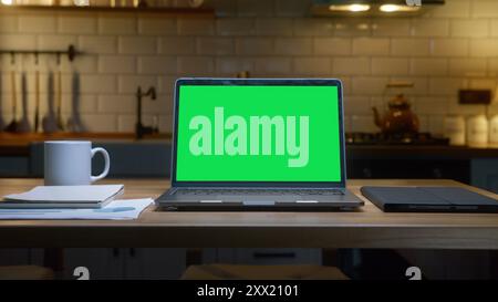 Un ordinateur portable avec un écran vert avec une tablette, une tasse à café et des documents sur une table en bois, mettant l'accent sur la productivité et l'organisation. Banque D'Images