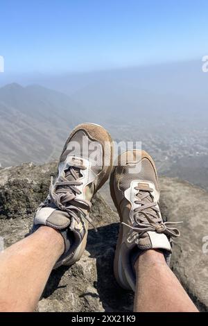 Une paire de chaussures sales reposent sur un sommet rocheux. Les chaussures sont usées et sales, et la personne qui les porte est détendue et profite de la vue Banque D'Images