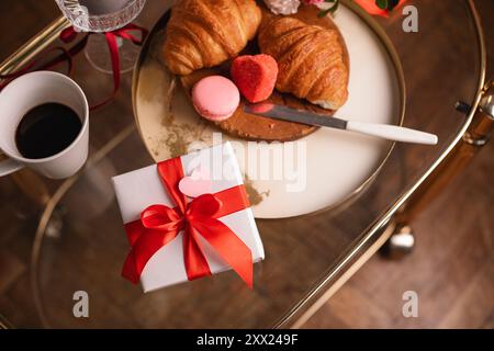 Vue aérienne d'un bouquet de fleurs et coffret cadeau sur une table avec une tasse de café, des croissants frais et des macarons pour un petit déjeuner Saint-Valentin Banque D'Images