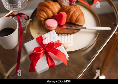 Vue aérienne d'un bouquet de fleurs et coffret cadeau sur une table avec une tasse de café, des croissants frais et des macarons pour un petit déjeuner Saint-Valentin Banque D'Images