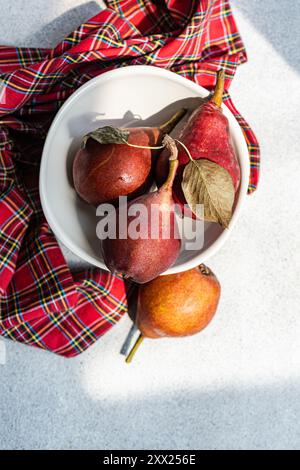 Vue aérienne de trois poires rouges Bartlett dans un bol sur une serviette à carreaux Banque D'Images