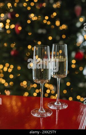 Gros plan de deux verres de champagne sur une table à côté d'un sapin de Noël illuminé Banque D'Images