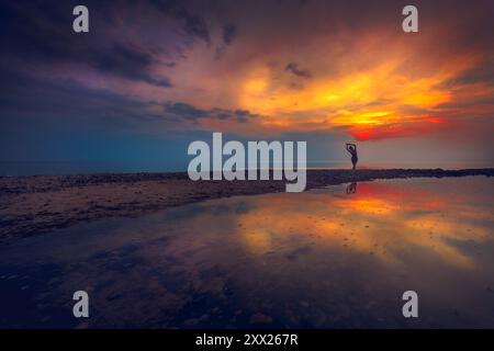 Vue arrière lointaine d'une jeune femme dansant sur la plage au coucher du soleil, Lituanie Banque D'Images