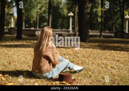 Vue de côté d'une femme assise sur l'herbe dans le parc en automne, Biélorussie Banque D'Images