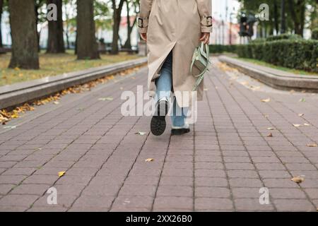 Vue arrière basse d'une femme dans un trench-coat marchant à travers le parc en automne, Biélorussie Banque D'Images