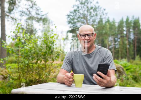 Homme finlandais senior utilisant le téléphone portable à l'extérieur dans un été de forêt scandinave en Finlande concept Banque D'Images