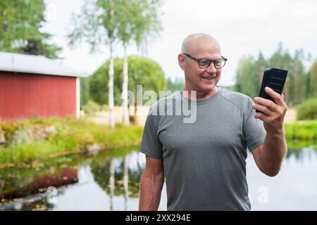 Homme finlandais senior utilisant le téléphone portable à l'extérieur dans un été de forêt scandinave en Finlande concept Banque D'Images