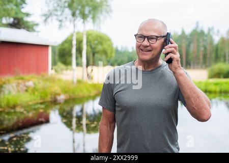 Homme finlandais senior utilisant le téléphone portable à l'extérieur dans un été de forêt scandinave en Finlande concept Banque D'Images