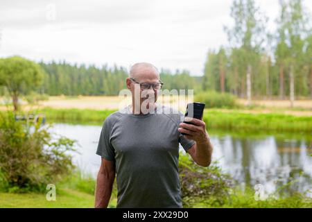 Homme finlandais senior utilisant le téléphone portable à l'extérieur dans un été de forêt scandinave en Finlande concept Banque D'Images