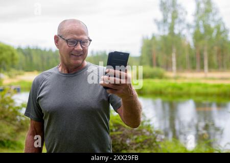 Homme finlandais senior utilisant le téléphone portable à l'extérieur dans un été de forêt scandinave en Finlande concept Banque D'Images