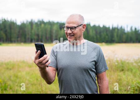 Homme finlandais senior utilisant le téléphone portable à l'extérieur dans un été de forêt scandinave en Finlande concept Banque D'Images