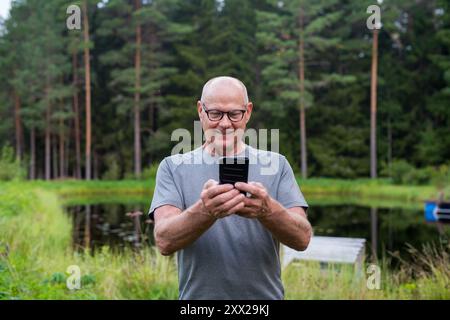 Homme finlandais senior utilisant le téléphone portable à l'extérieur dans un été de forêt scandinave en Finlande concept Banque D'Images