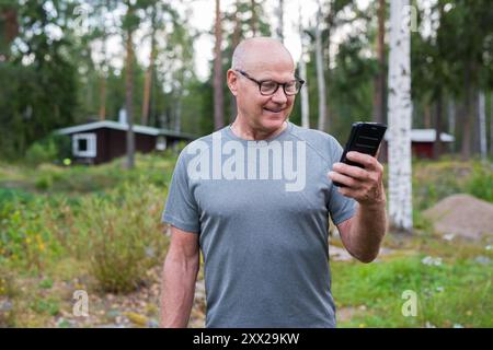 Homme finlandais senior utilisant le téléphone portable à l'extérieur dans un été de forêt scandinave en Finlande concept Banque D'Images