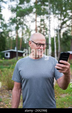 Homme finlandais senior utilisant le téléphone portable à l'extérieur dans un été de forêt scandinave en Finlande concept Banque D'Images