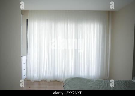 Cette chambre lumineuse présente des rideaux transparents et un décor minimaliste, créant une atmosphère sereine Banque D'Images