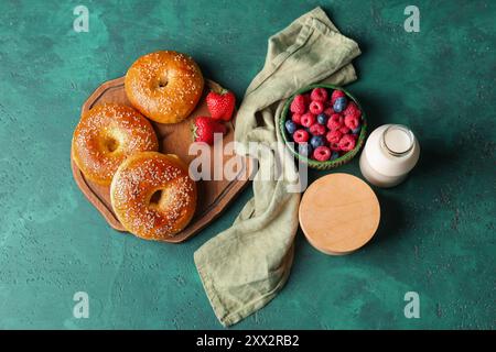 Planche en bois avec des bagels savoureux, des baies et une bouteille de lait sur fond vert Banque D'Images