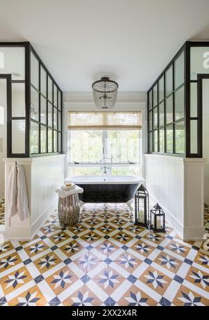 Salle de bains élégante avec baignoire sur pieds à griffes noire et blanche et fenêtres encadrées en métal autour de la douche et des toilettes Banque D'Images