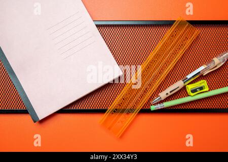 Une règle, un crayon et un stylo se trouvent sur une table à côté d'un bloc-notes. Le carnet est rose et a une grille sur les pages Banque D'Images