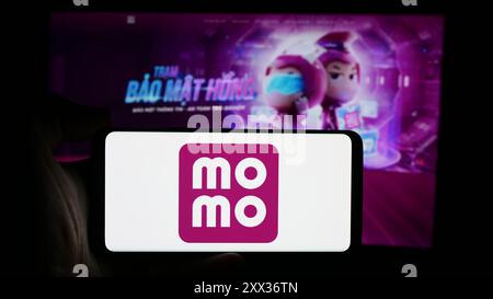 Personne tenant le téléphone portable avec le logo de la société fintech vietnamienne MoMo en face de la page Web de l'entreprise. Concentrez-vous sur l'affichage du téléphone. Banque D'Images