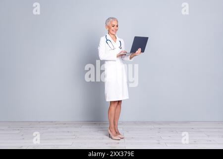 Photo de charmant médecin professionnel attrayant chirurgien spécialiste qualifié tenir l'utilisation netbook isolé sur fond de couleur grise Banque D'Images
