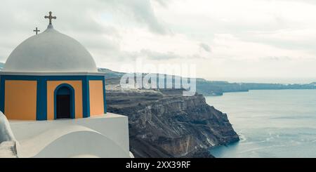 Santorin, Grèce - 8 octobre 2019 : église emblématique au dôme bleu surplombant la mer Égée. Banque D'Images