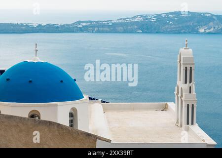 Santorin, Grèce - 8 octobre 2019 : église emblématique au dôme bleu surplombe la mer Égée. Banque D'Images