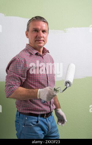 Un homme peint des murs verts avec de la peinture blanche avec un rouleau. Travaux de construction et réparations cosmétiques dans la maison, peinture des murs, travaux de finition avec votre ow Banque D'Images